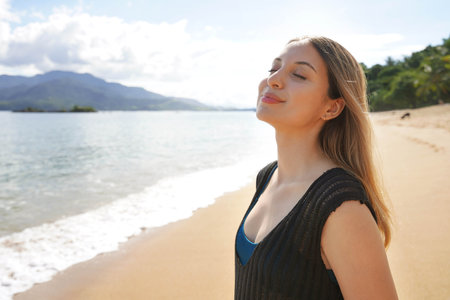 Portrait of young lady breathing with closed eyes enjoys sunbathe on the beach. Relax and sunbathing in Ilhabela Island, Brazil.の写真素材