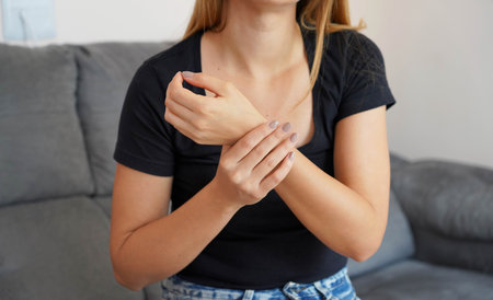 People, healthcare and problem concept. Unhappy young woman suffering from wrist pain sitting on sofa at home.の写真素材