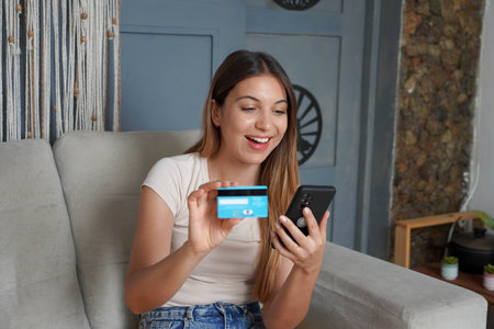 Cheerful and satisfied Brazilian woman doing shopping online sitting on sofa at home. Latin girl...