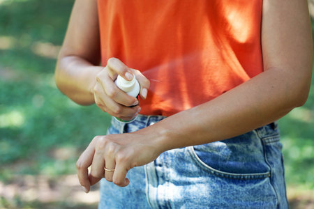 Girl spraying insect repellent on her arm outdoor in nature using spray bottle. Mosquito repellent. Bug spray anti insects.の写真素材