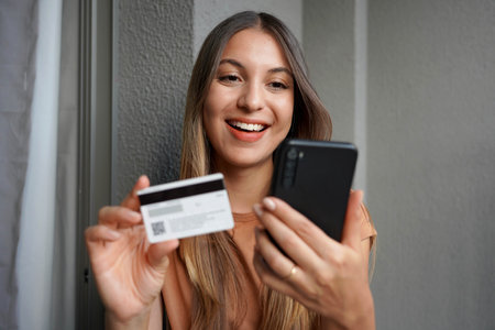 Close-up of attractive hispanic girl makes purchase on smartphone with credit cardの写真素材