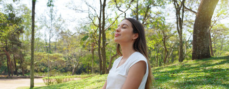 Relaxed young woman breathing fresh air in a city park. Panoramic banner view.