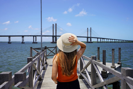 Tourism in Aracaju, Brazil. Back view of young woman on pier in Aracaju with Ponte Joao Alves bridge on the background, Brazil.の写真素材