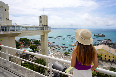 Tourism in Salvador de Bahia, Brazil. Traveler girl on terrace enjoying viewpoint with Lacerda Elevator and harbour of Salvador de Bahia, Brazil.の写真素材