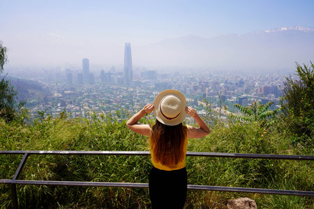 Happy traveler woman enjoyong view of Santiago de Chile skyline with Andes Mountains from lookout, Santiago, Chileの写真素材