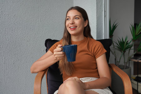 Hispanic young woman relaxing with hot drink on armchair at home