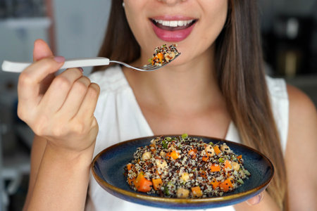 Unidentified girl eating a warm quinoa salad with carrots, broccoli and chickpeas. Focus on the...