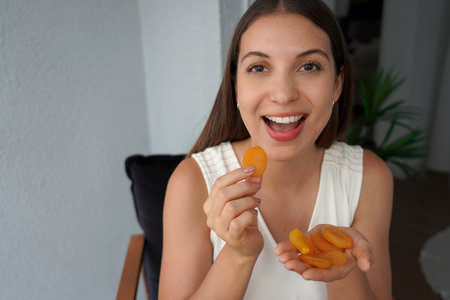 Healthy young woman eating apricots dried in the morning. Looks at camera.