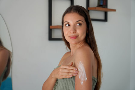 Brazilian young woman applying cream onto shoulder at homeの写真素材