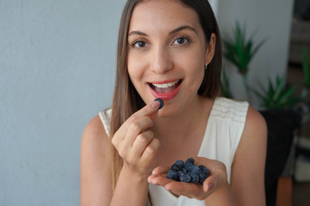 Beautiful young woman picking a blueberry from her hand. Looking at camera.の写真素材
