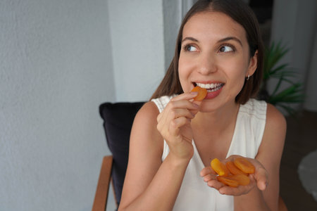 Hispanic girl biting apricots dried at home.の写真素材