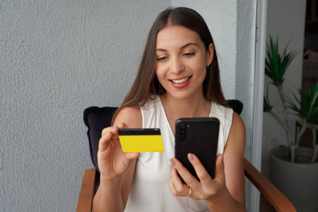 Hispanic girl reading and inserts credit card number on phone to complete online order while sits on...