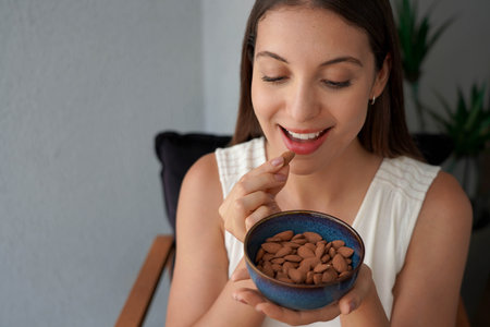 Beautiful healthy young woman eating almonds unpeeled as snack at home. Looking down. Copy space.の写真素材