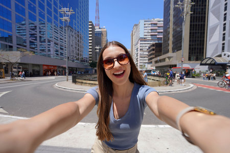 Happy young woman with sunglasses taking a wide-angle selfie on a sunny day in Sao Paulo, Brazil