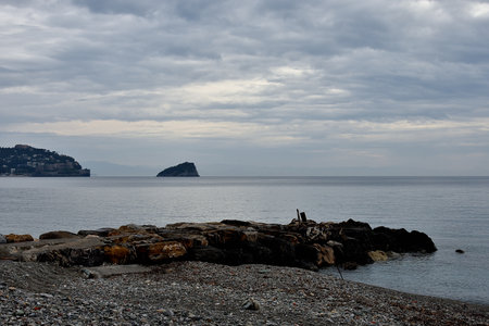 A vertical shot of a man sitting on a rock by the sea under a cloudy skyの写真素材