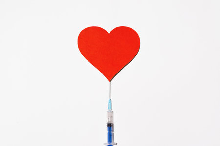 Syringe with vaccine and a big red heart on a white background, top view. Safe vaccination conceptの写真素材