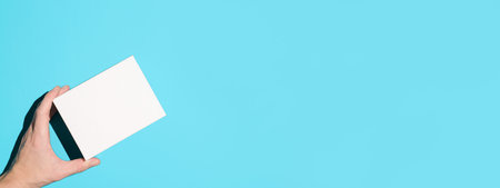 Hand holding small white box on blue background, top view. Mock up, empty space for a logo. Delivery banner, copy spaceの写真素材