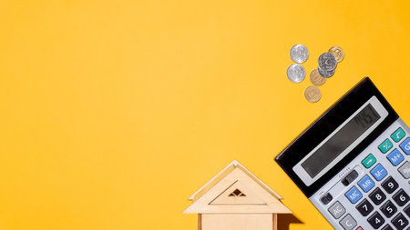 Coins, calculator and toy house, top view. Yellow background, copy space. Concept of rent payment, loss of income, mortgage debtの写真素材