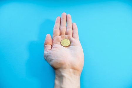 A man holds one coin in his palm, close-up. Fifty cents euro in hand, POV. Bankruptcy, poverty, falling income, low cost. blue backgroundの写真素材