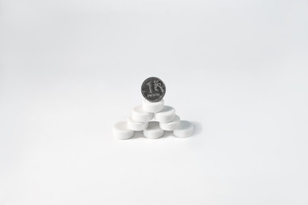 The coin stands on a mountain of tablets, white background. Pyramid of pills and one ruble. Medicine and healthcare budget, drug prices, treatment costs.の写真素材