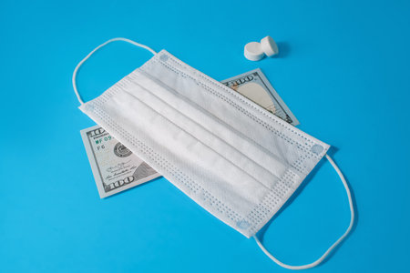 Dollar under a medical face mask, pills, on a blue background. Symbolizes the global recession, the...