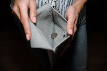 A woman shows a wallet with one coin, close-up. The concept of bankruptcy, income decline, poverty, unemployment. Selective focus, dark backgroundの写真素材