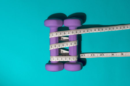 Purple dumbbells and tape measure on a blue background. Fitness concept, weight loss, diet.の写真素材