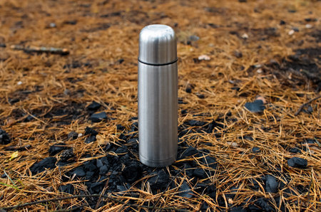 flask in the forest stands on coals. Background of fallen yellow Christmas-tree needles. Concept for hiking, travel, hot drink in cold weather.の写真素材