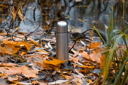 Vacuum steel flask outdoors. Hiking flask stands by the water. Hike concept, relaxation in nature, hot drink in cold weather.の写真素材