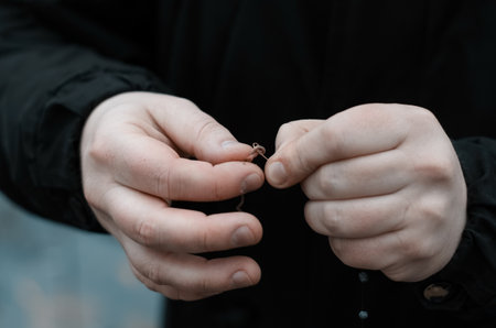 Man fishing in a wild lake. Male hands baiting a worm on a hook, close up. Autumn fishing in cold...