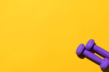 Dumbbells on a yellow background, copy space. Top view, flat lay. Two purple dumbbells for fitness and aerobics.の写真素材