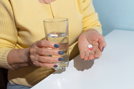 Elderly woman drinking pills. Close-up of female hands holding glass of water and medicine. treatment concept, sickness retirementの写真素材