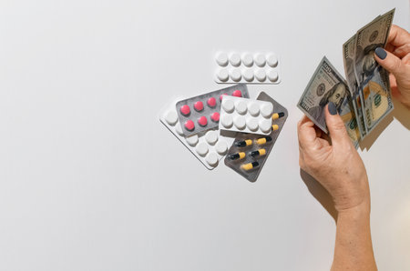 Elderly woman's hands holding money. Tablets on white table top view, copy space. Concept of treatment cost, medicine price, health insurance budgetの写真素材