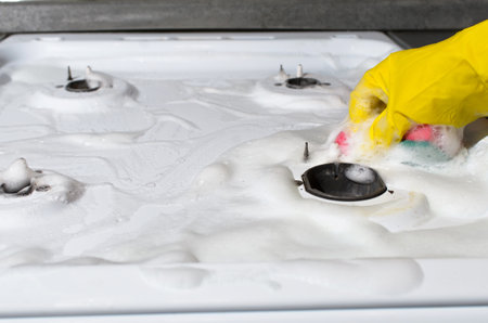 Woman cleans gas stove close-up. Female hand in glove washing gas panel with sponge. Hygienic kitchen cleaningの写真素材