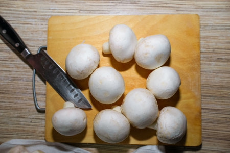 Top view of champignon mushrooms lying on cutting wooden board in kitchen, indoorsの写真素材