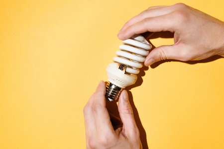 Male hands holding a burnt out light bulb. Yellow background, top view. electrician conceptの写真素材