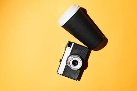 Retro film camera and disposable cup of coffee. Yellow background, flat lay. photo walk conceptの写真素材
