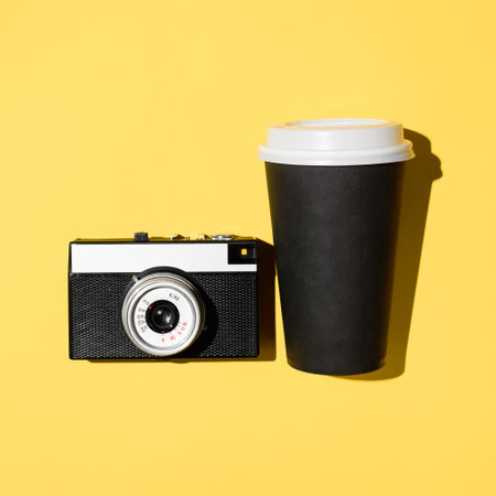 Retro film camera and disposable cup of coffee, close-up. Yellow background, flat layの写真素材