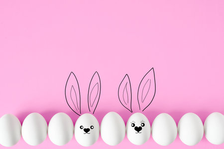 Easter background. White eggs lying in row on pink background, flat lay. Drawn rabbit face with ears. Romantic concept with cute bunny eggs, copy space. happy easter holidayの写真素材