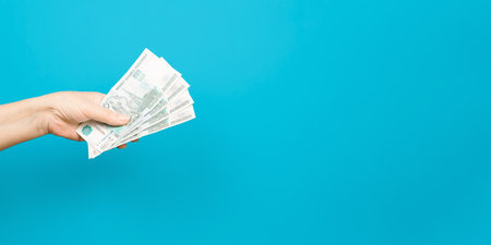 Senior woman's hand holding out money on a blue background indoors, copy space. Thousands of rubles.の写真素材