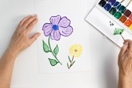 Senior woman's hands painting flower in watercolor. First person view. Woman creating palette with paintbrushの写真素材