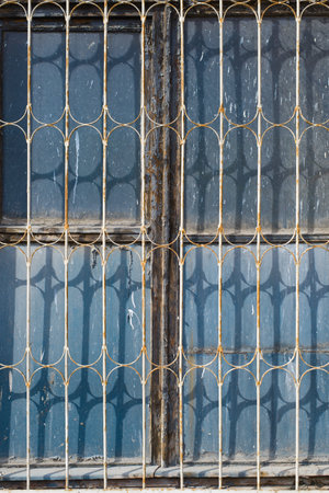 An old, dirty window behind bars outside. vertical photo