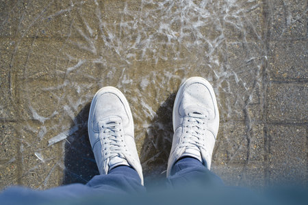 A man in sneakers stands on the cracked ice. Top view from the first person. frozen puddleの写真素材