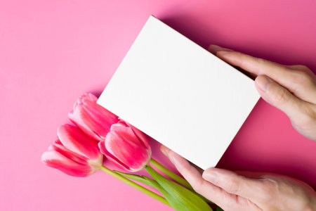 Male hands holding out white gift box and flowers on pink background. Flat lay, copy space. Layout with place for text.の写真素材