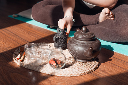 Tea ceremony indoors in the morning. Woman in lotus position holding a small teapot, close-upの写真素材