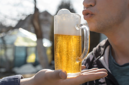 Man wants to drink foamy beer, pulls his lips to the mug, outside. Close-up, selective focus....