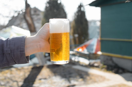 Male hand holding a mug of beer in a vegetable garden outside on a sunny day. Close-up, selective focus.の写真素材