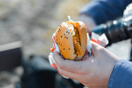 Man eating a burger outside on a sunny day. Close-up of male hand holding fast food, selective focusの写真素材