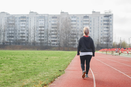 Middle-aged woman practicing race walking in a street stadium, back view. Active lifestyle, weight loss conceptの写真素材