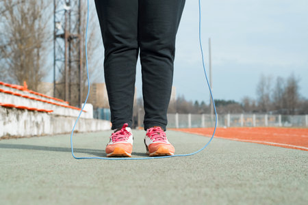 Woman doing sports at the stadium. Women's legs in sneakers for running and a jump rope, close-up. Skipping rope training. Croppingの写真素材
